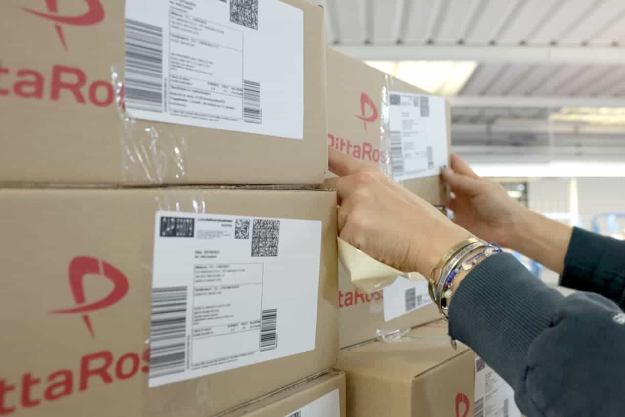 hands handling Pittarosso branded packages with shipping labels in the warehouse.